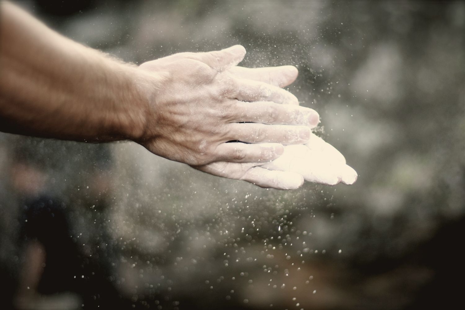 Close-up of chalked hands, chalk dust floating in the light.