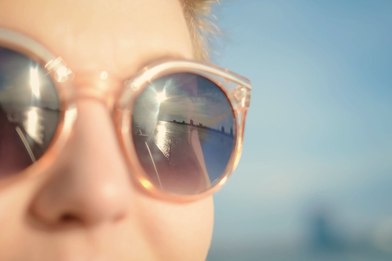 Close-up of rose-tinted sunglasses reflecting sun and water.