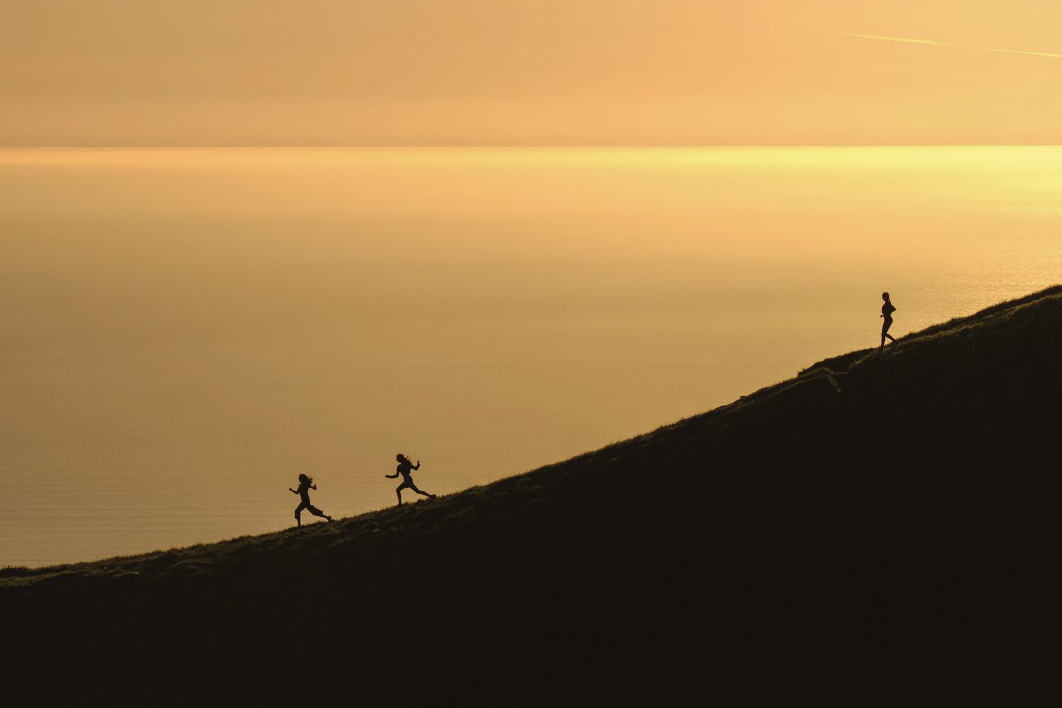 Three runners silhouetted on a ridge above a golden sea.