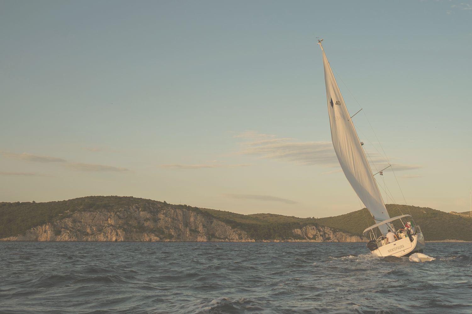 A yacht heeling in the wind off a rocky island.
